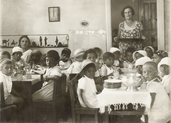 JDC's increased allotments made it possible to provide children better care, including supplemented nourishment, new winter and summer clothing, and where needed, more sanitary quarters. In a Yemenite kindergarten in Neve Sha'anan, Jerusalem, wholesome lunches helped restore these youngsters to good health. Palestine, c. 1920, <em>NY_00005</em>.
