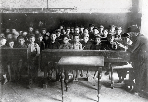 Where possible, JDC subsidized Jewish schools during the war. Many schools were forcibly abandoned, and refugee children had little opportunity for education. In the post-war years, the number of institutions receiving support increased. The Central Committee's funds supported talmud torahs and yeshivot. The melamed of a JDC-supported cheder instructed his pupils. Poland, c. 1918, <em>NY_01412</em>.
