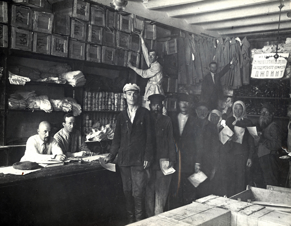 In October 1921, postal connections between Russia and the US were reestablished. ARA cleared the way for $10 food packages to be purchased in America and sent to individuals in famine-struck areas of the Soviet Union. JDC quickly began gathering subscriptions from American Jews for their needy relatives and friends. By December 1922, around $8 million worth of sugar, rice, vegetable oil, tea, flour, and canned milk had been shipped. As ARA required, half the packages went to non-Jews. Clients lined up to receive their packages in JDC’s warehouse in Kremenchug. Ukraine, c. 1922, <em>NY_00446</em>.